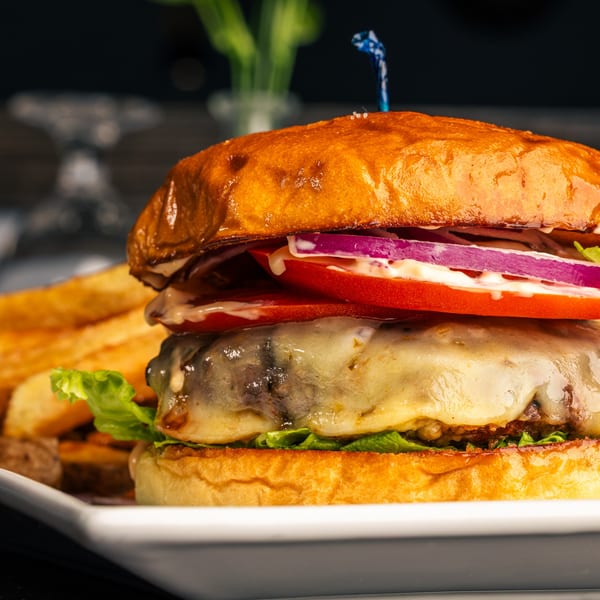 Close-up of a Maura's Kitchen burger with melted cheese, lettuce, tomato, and red onion, served with fries.