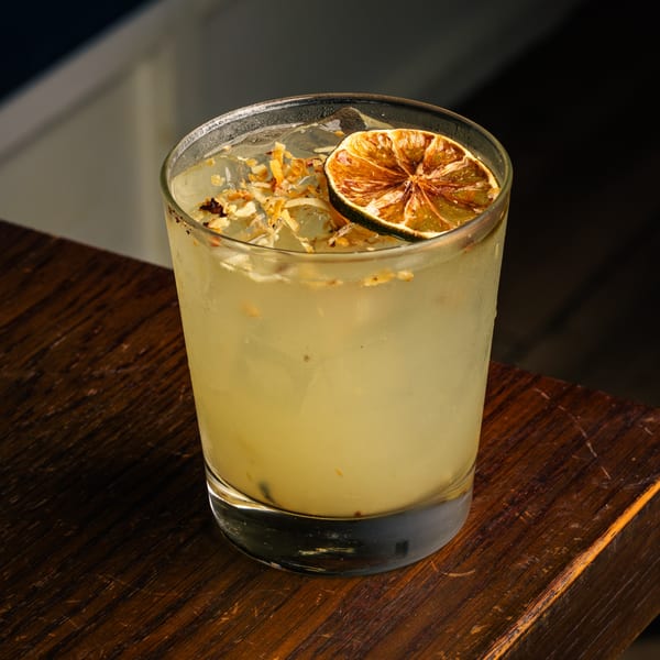 Peruvian cocktail with a dried lime and coconut flakes, served in a glass on a wooden table.