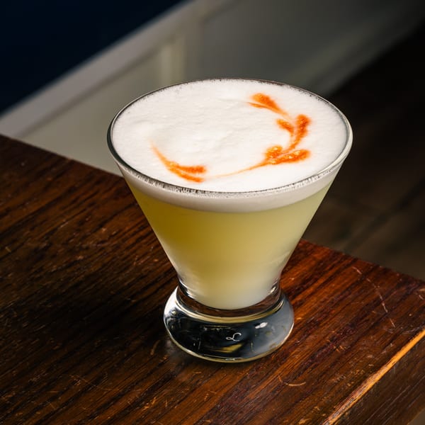 Peruvian Pisco Sour cocktail with a foamy top and an orange garnish, on a wooden surface.
