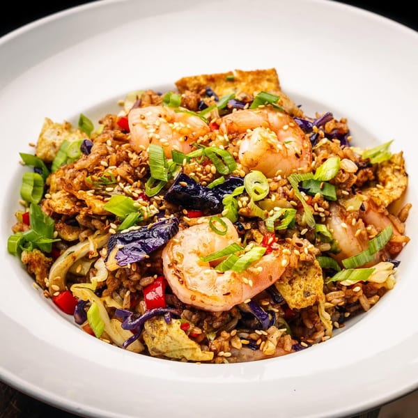 Peruvian chaufa de mariscos with shrimp, rice, vegetables, and sesame seeds in a white bowl.