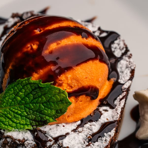 Peruvian chocolate cake with orange ice cream, chocolate syrup, powdered sugar, and a mint leaf.