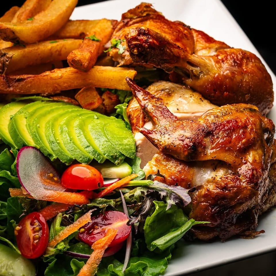 Peruvian rotisserie chicken with crispy fries, sliced avocado, and a fresh garden salad.
