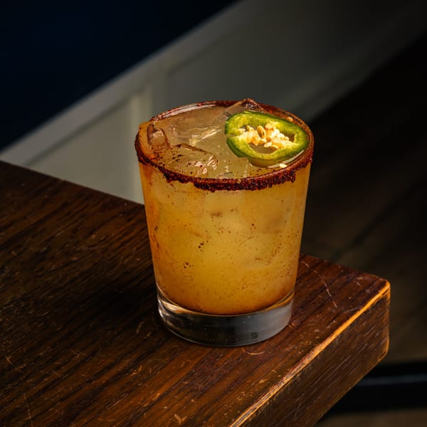 Spicy Peruvian cocktail with a chili-dusted rim and a jalapeño slice on a wooden surface.