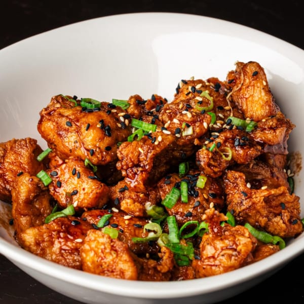 Peruvian fried chicken bites, glazed with a dark sauce, topped with sesame seeds and green onions.