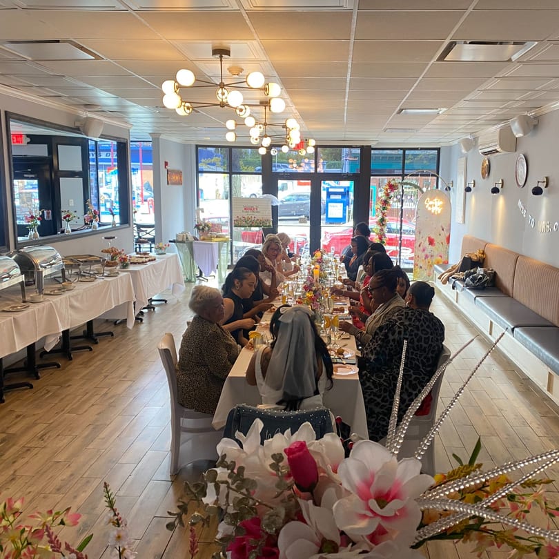 Women gather for a bridal shower brunch at a long table in a modern restaurant.