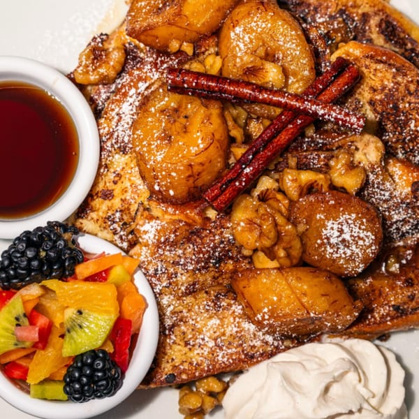 Maura's Kitchen French toast with caramelized bananas, walnuts, cinnamon sticks, fruit salad, and syrup.
